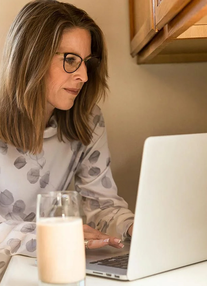 Woman using her computer in the kitchen counter drinking a glass of milk