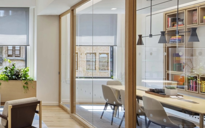 <span class="uk-h4">Meeting room shown through floor-to-ceiling glass sliding doors. Automated shades are partially lowered in the background.</span>